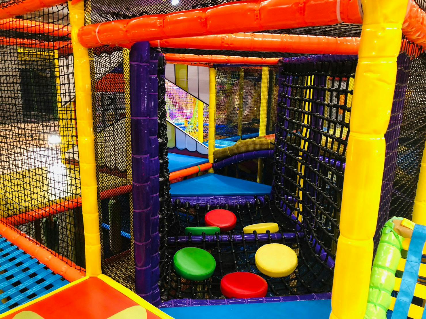 A colorful indoor play structure with nets, padded climbing areas, and round seats in primary colors.