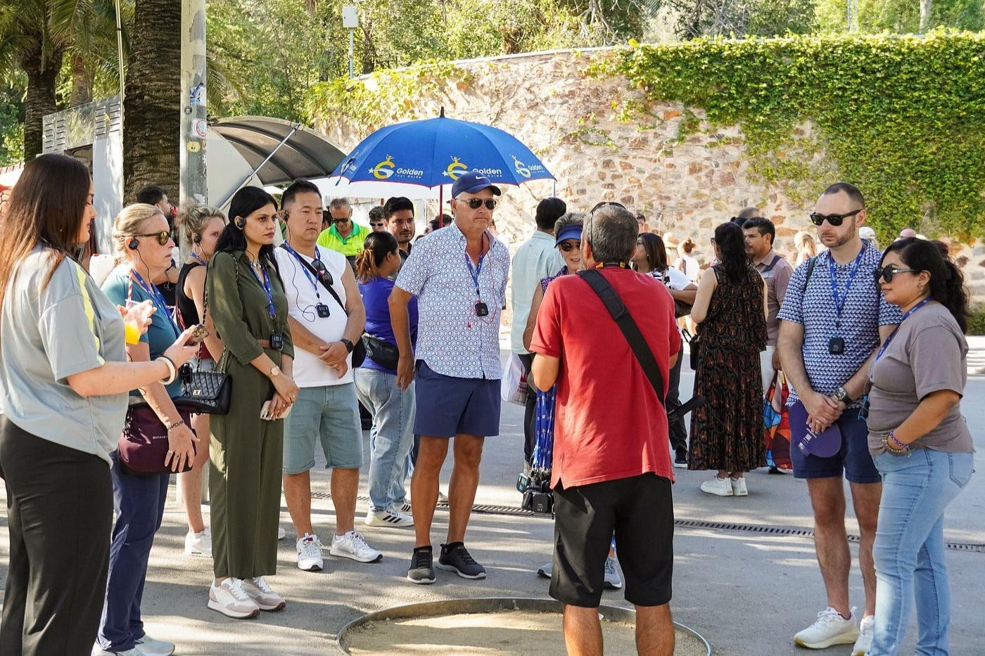 Un groupe de personnes s'est rassemblé en plein air, certaines portant des casques audio, une personne tenant un parapluie bleu avec un logo.
