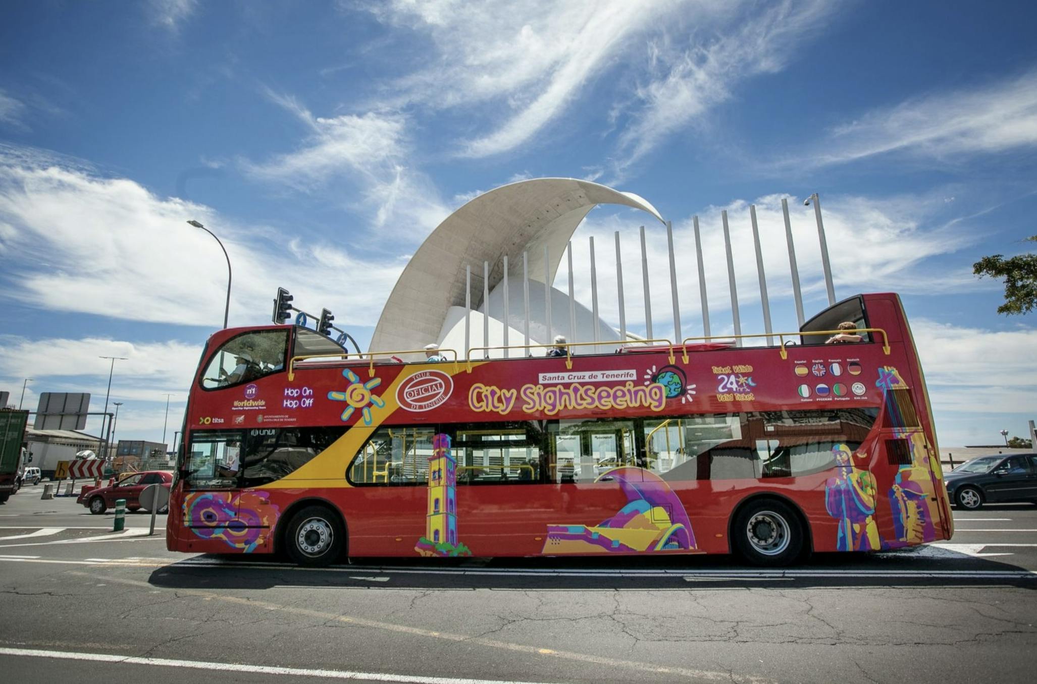 A red double-decker tour bus labeled "City Sightseeing" in front of a modern white building with arched features under a blue sky.