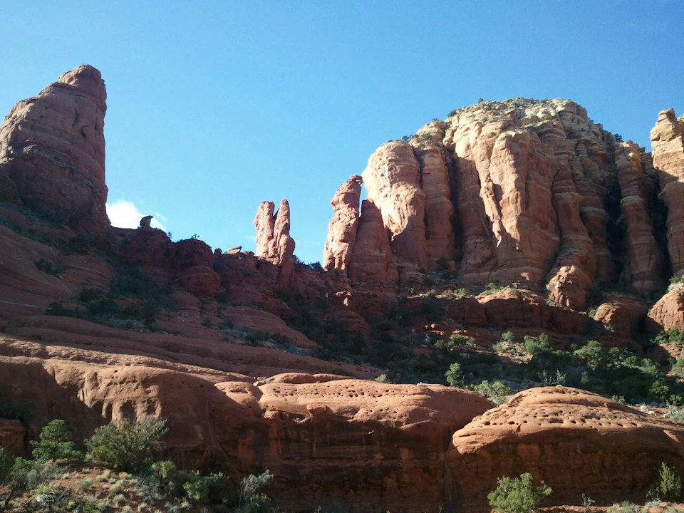 Sunlit red rock formations with sparse vegetation under a clear blue sky.