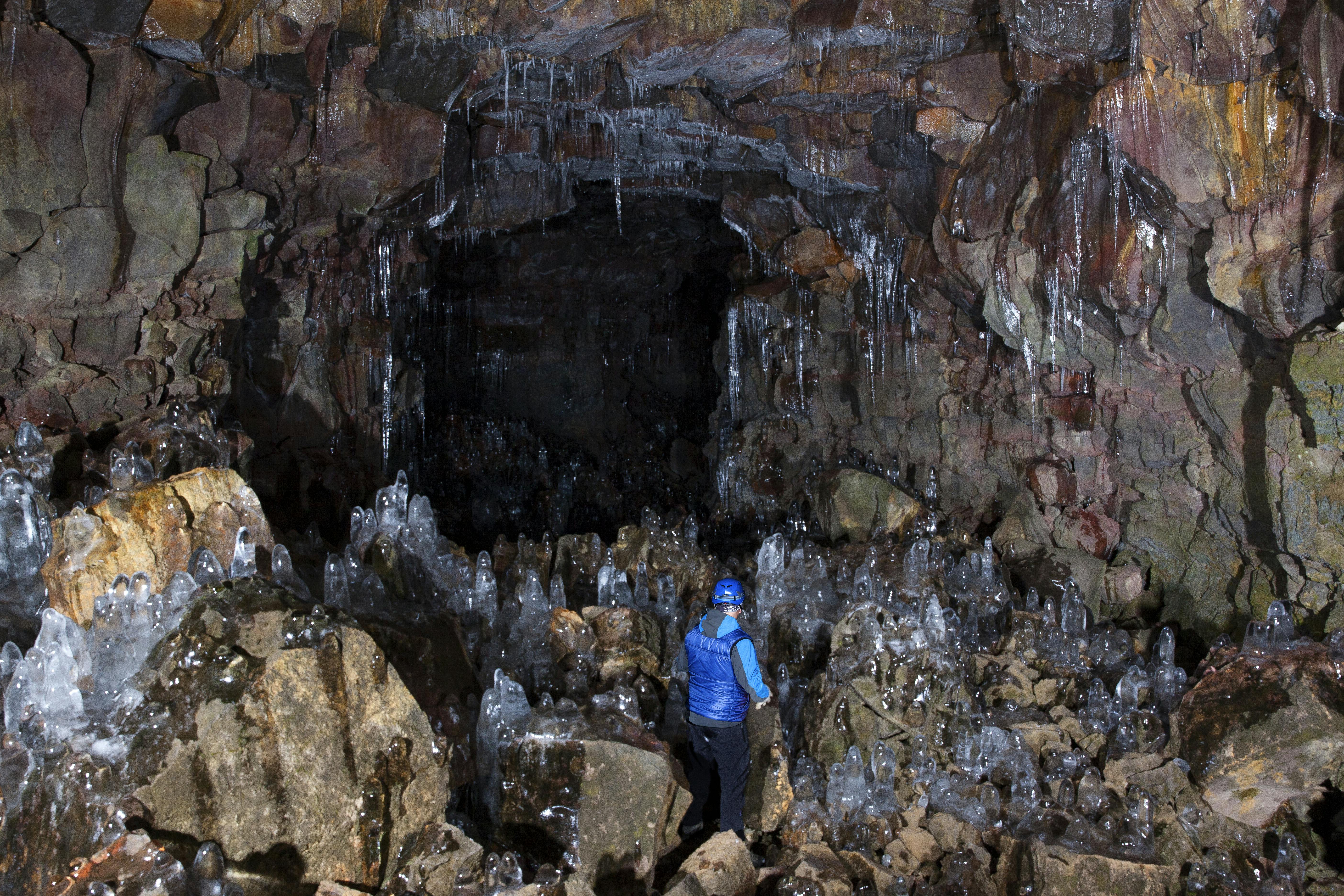 Person wearing a blue jacket and cap standing in a cave with icy stalagmites and icicles hanging from the ceiling.