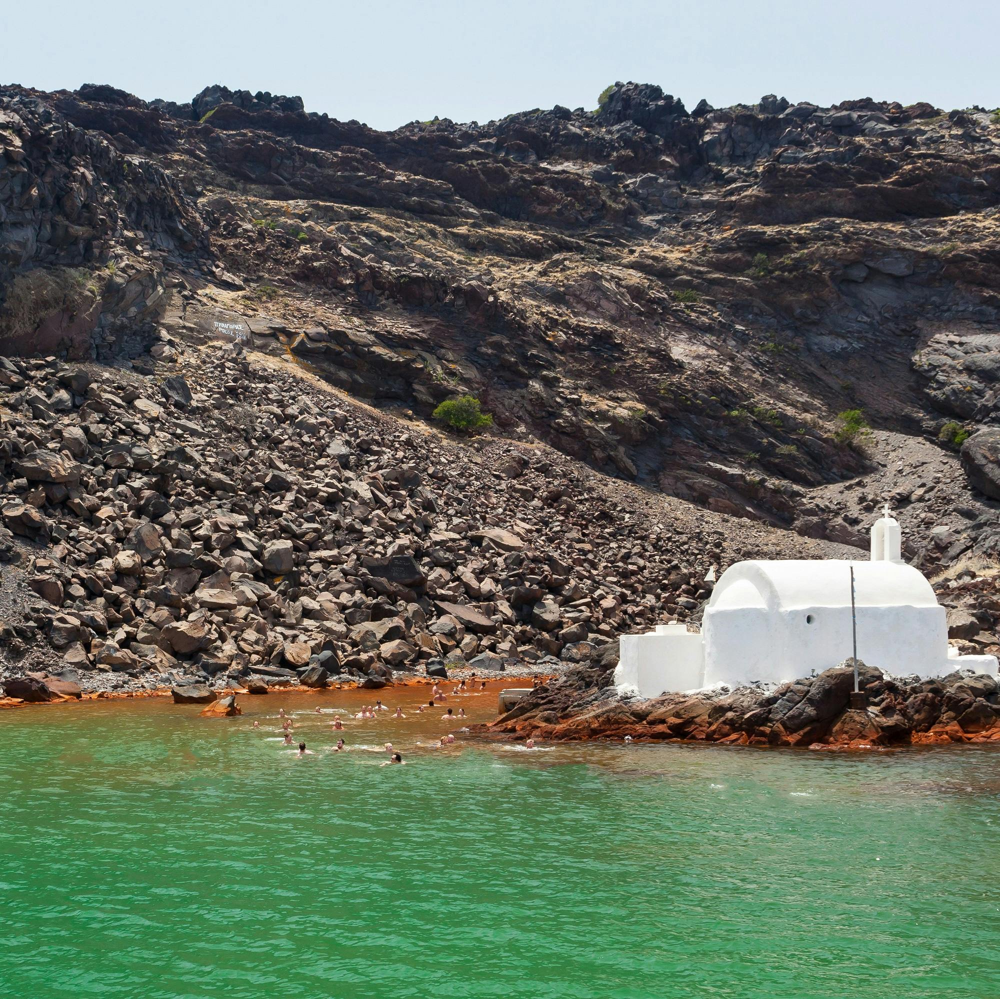 푸른 물에서 수영하는 사람들과 함께 바위 언덕 근처의 하얀 건물.
