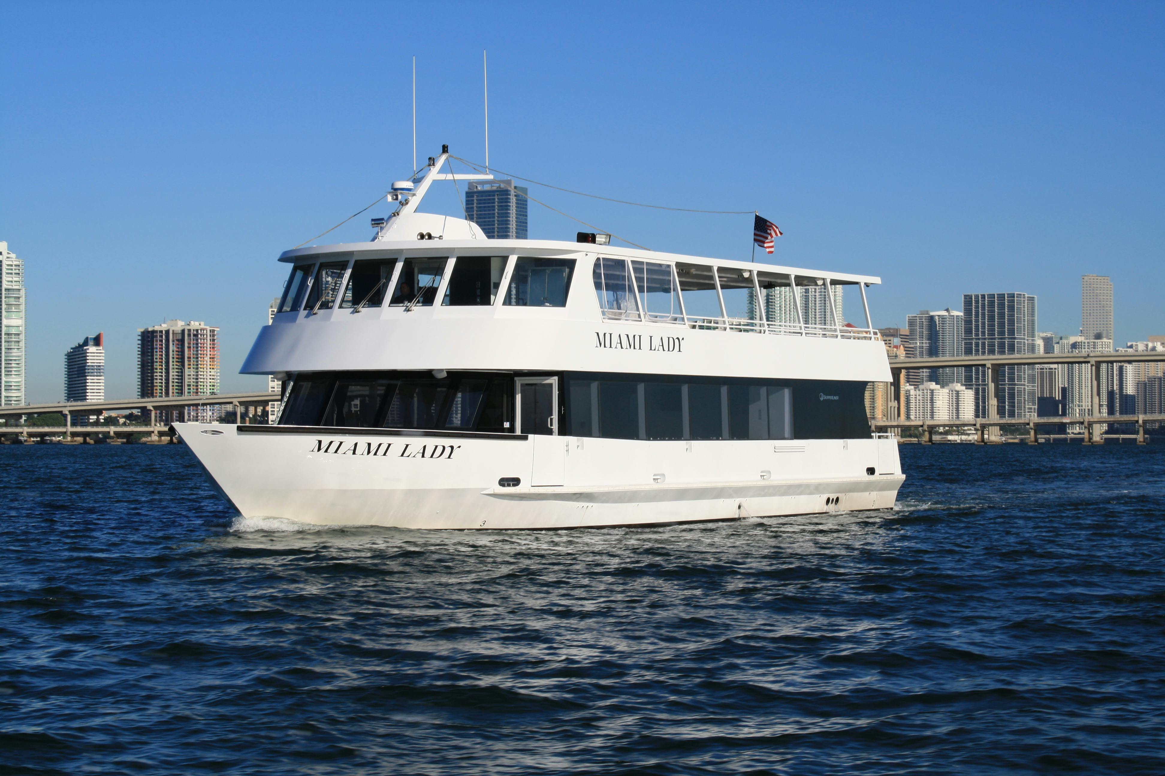 Yacht bianco di nome "Miami Lady" in tour in barca con paesaggio urbano e cielo azzurro sullo sfondo.