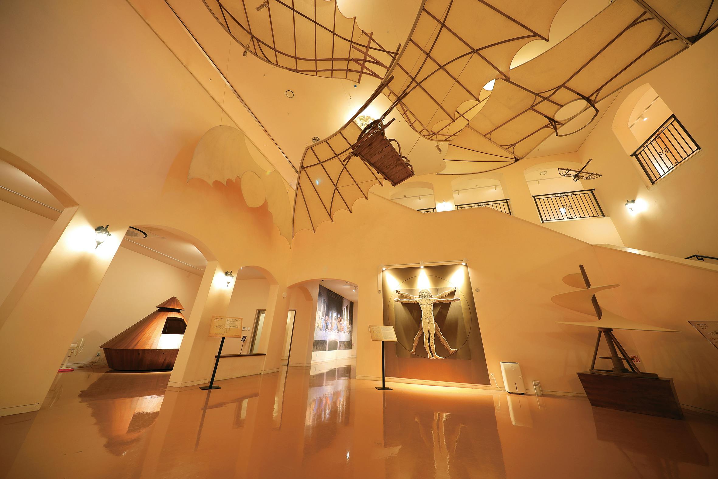 A museum exhibit featuring a large flying machine model suspended from the ceiling and a Vitruvian Man-inspired artwork on the wall.