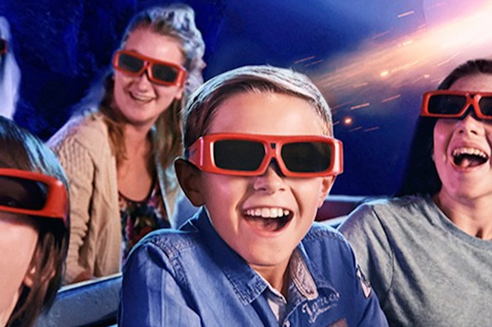 A group of people wearing 3D glasses, smiling and laughing, with a dynamic, glowing backdrop suggesting a theme park ride.