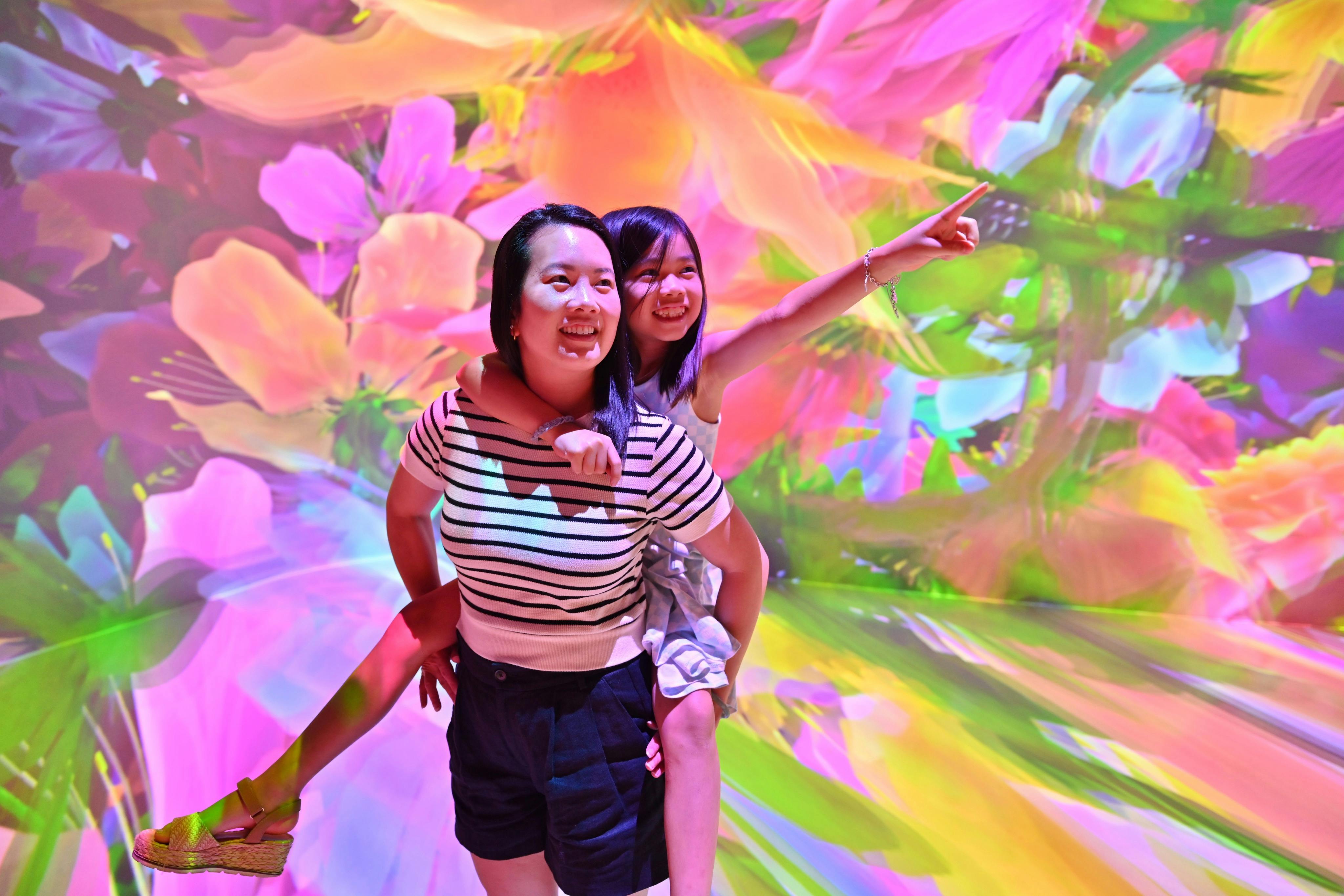 Dues persones posant alegrement sobre un fons vibrant de patrons florals colorits i abstractes.