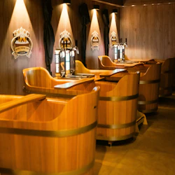 Träkar med ölkranar på ett Beer & Wine Spa upplyst av strålkastare, med logotavlor på väggen och mörka gardiner.
