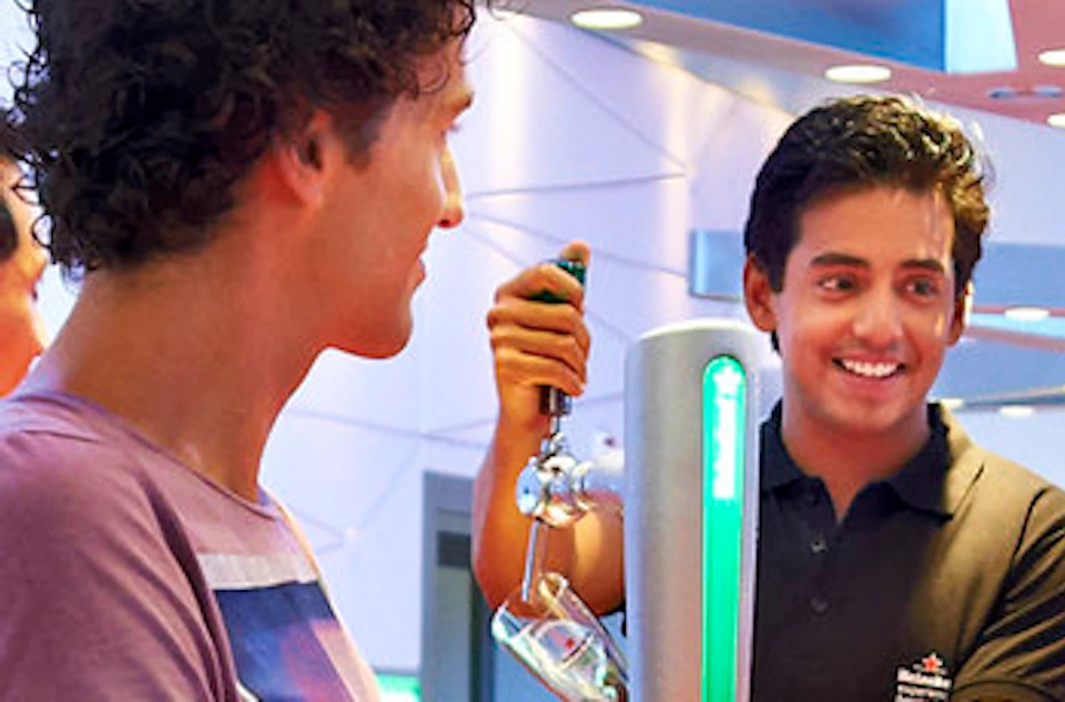 People socializing at a modern bar with red counters and metal structures overhead, holding drinks and engaging in conversation.