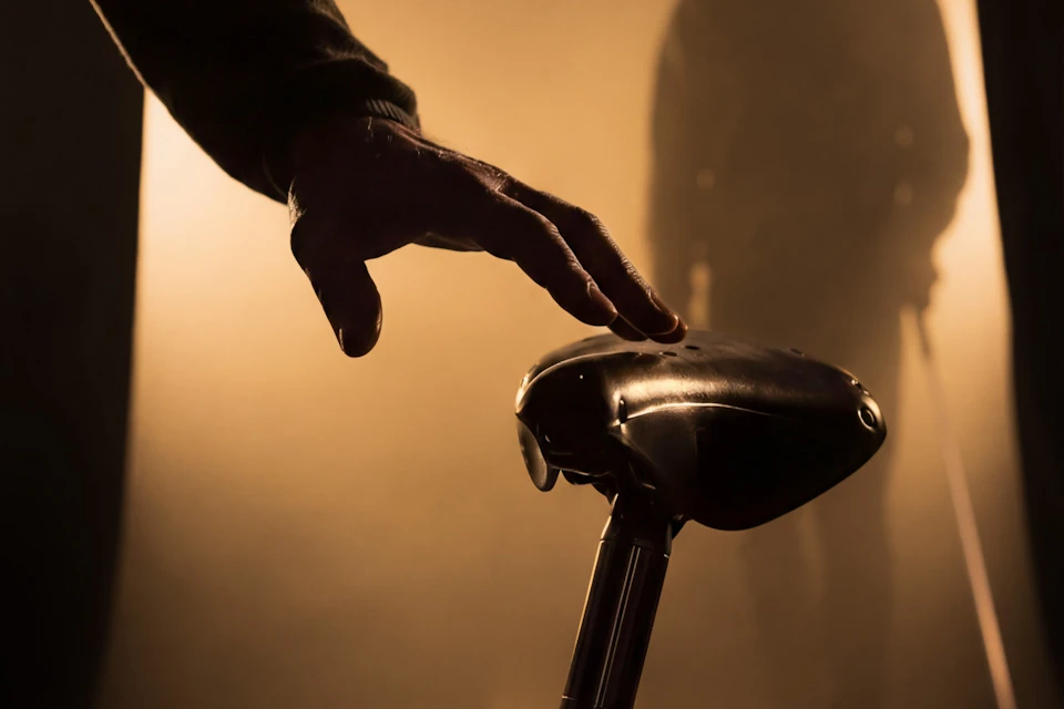 A hand reaching towards a bicycle saddle in a dimly lit, moody environment.