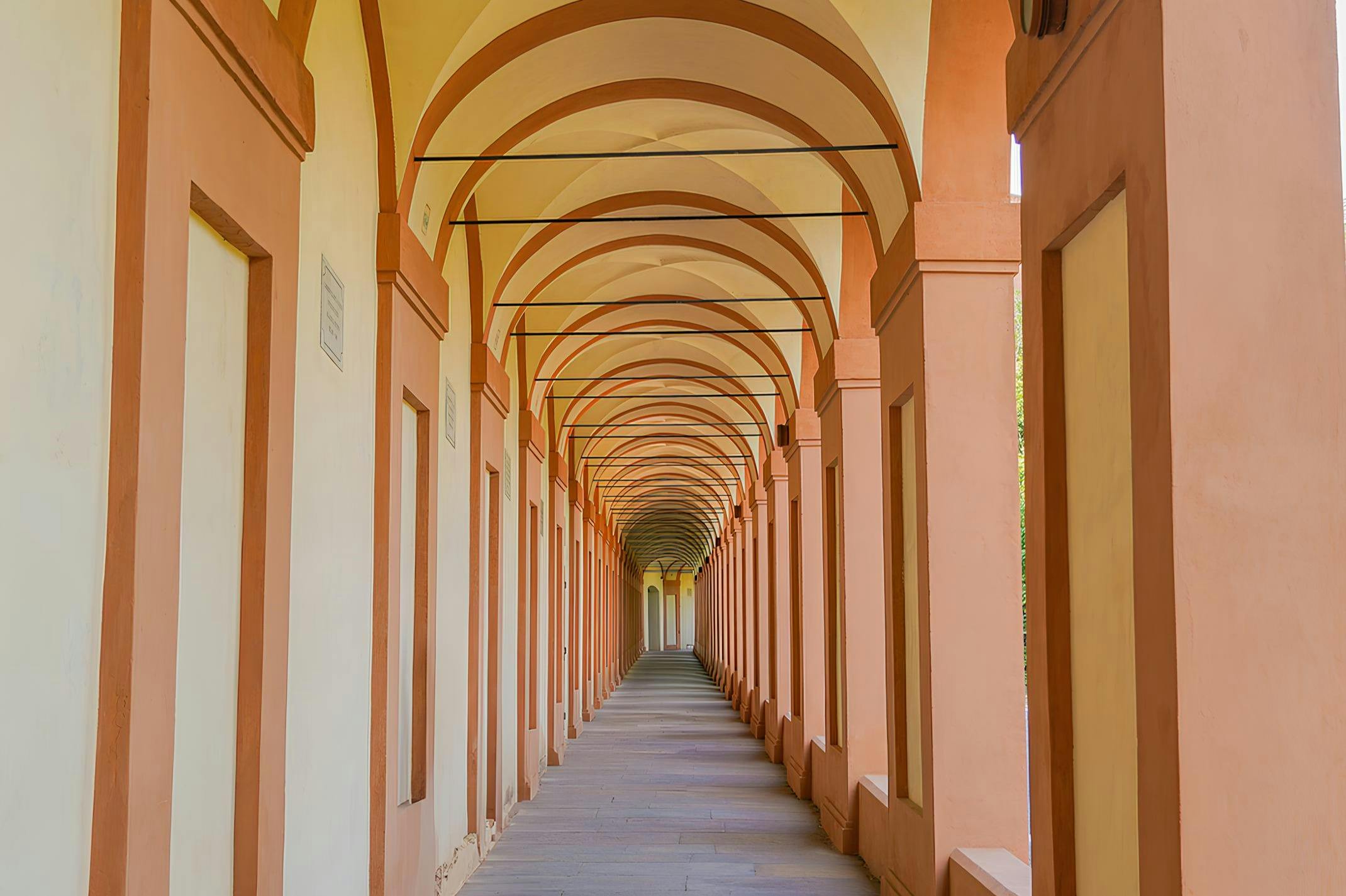 A long, covered walkway with repetitive archways and columns in shades of orange and beige.