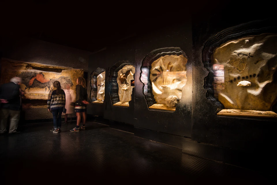 A dimly lit exhibit with rock formations and silhouettes of two people viewing displays in a museum-like setting.