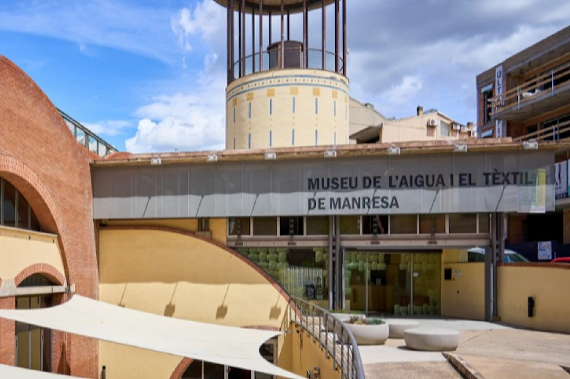 Modern building labeled Museu de l'Aigua i el Tèxtil de Manresa, featuring a tower and a courtyard with seating.