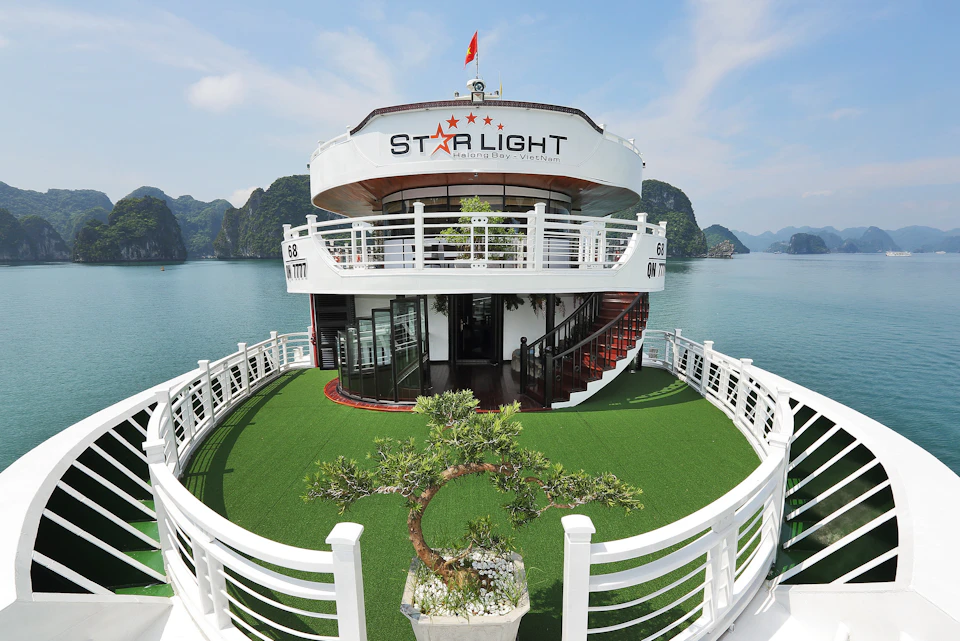 A boat named "Starlight" with a landscaped green deck, a potted tree, white railings, and stairs in front of scenic, mountainous water views.