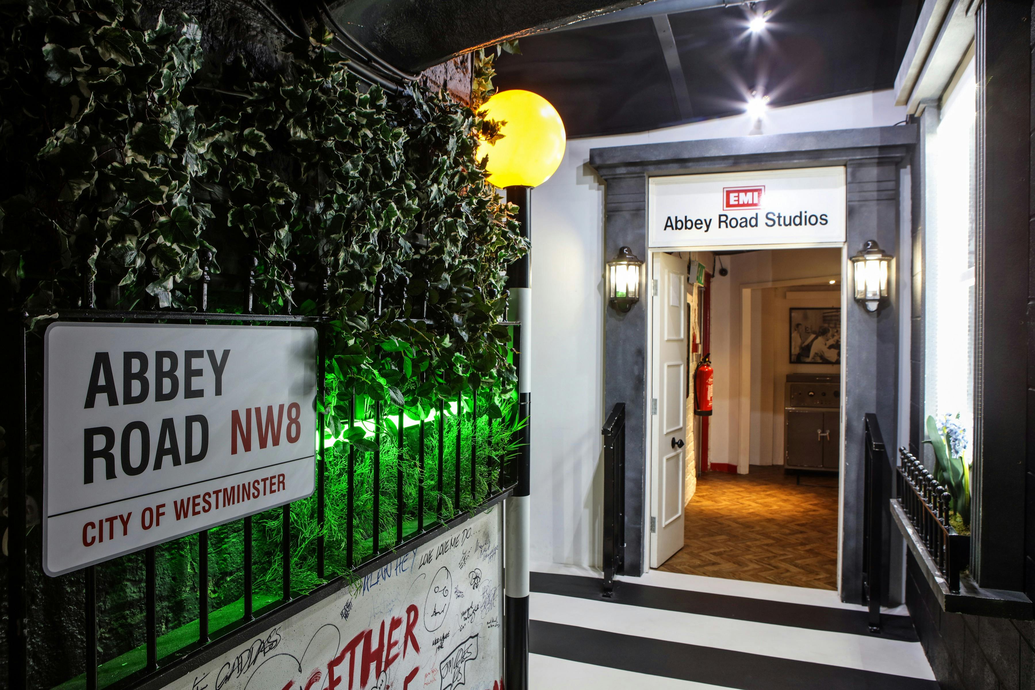 Indgang til Abbey Road Studios med et gadeskilt, en mur dækket af vedbend og en glødende gul lampe.