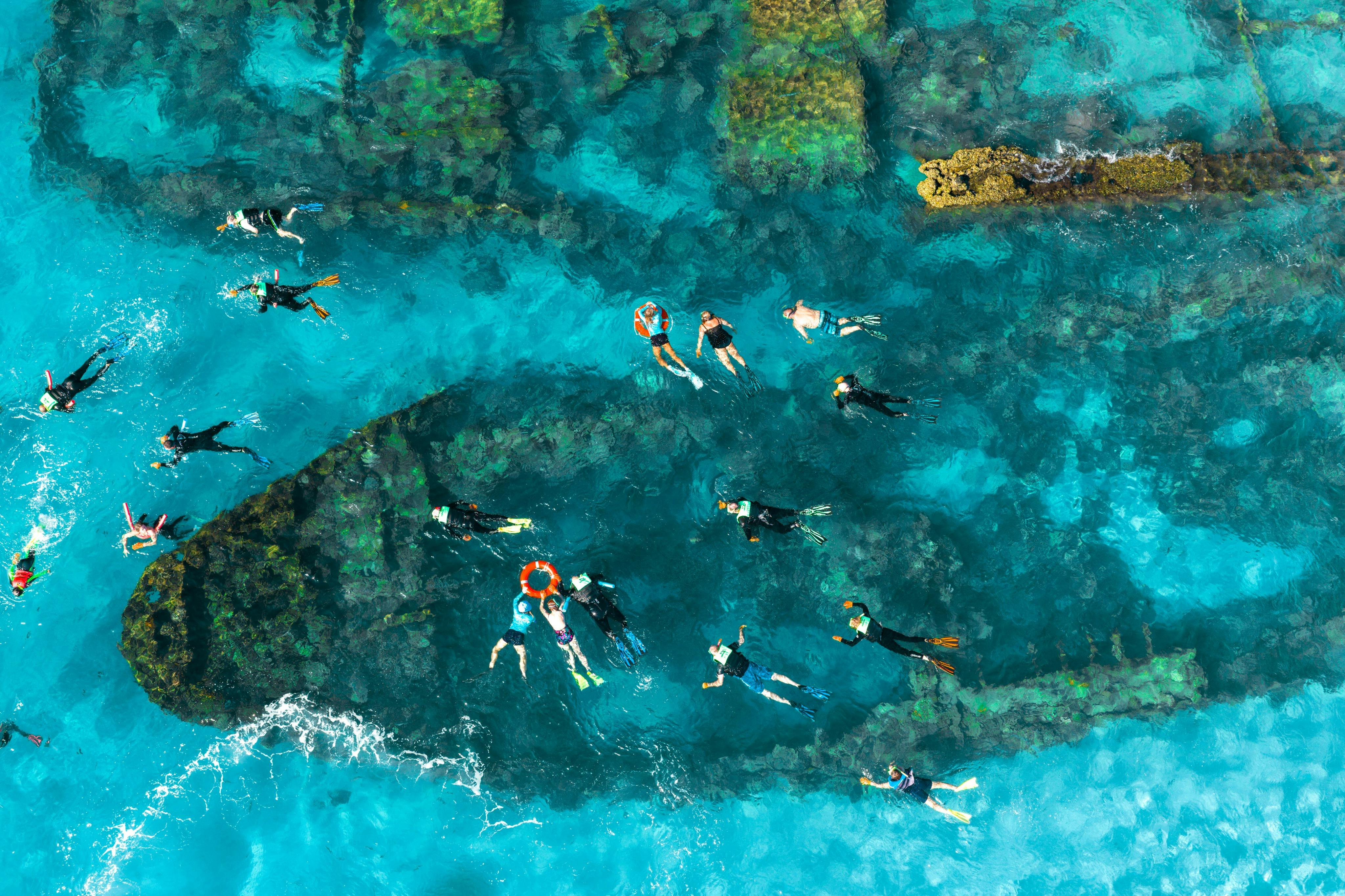 Mensen snorkelen in helder turquoise water boven onderwaterriffen, van bovenaf gezien.