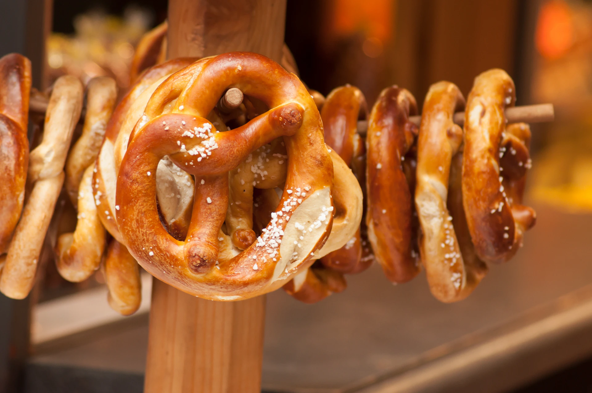 Soft pretzels with coarse salt are hung on wooden pegs in a display.