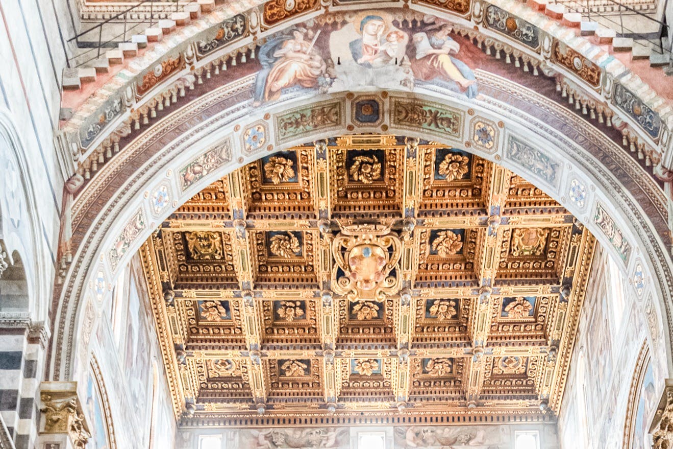 Ornate, coffered ceiling with intricate, gold carvings and a painted arch featuring religious figures.