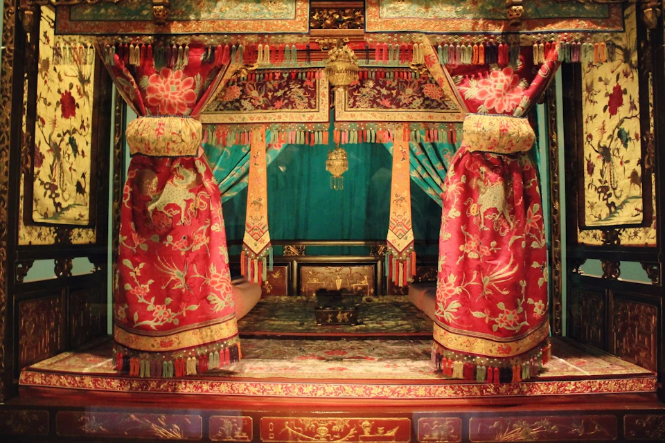 Ornate, colorful room with intricate red and gold drapes framing a cushioned seating area and decorative gold elements.
