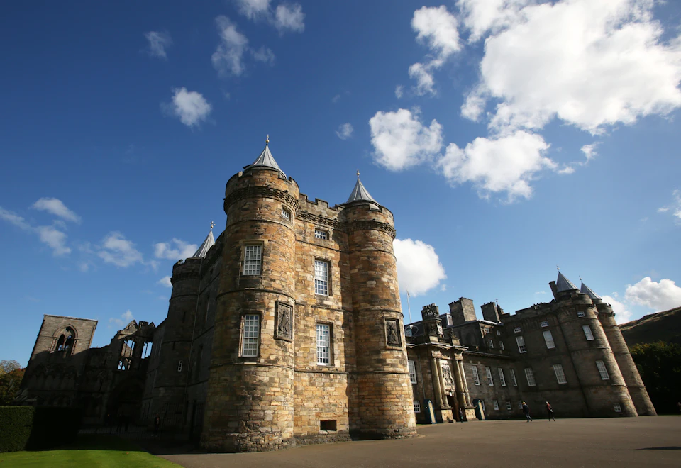 Stone castle with round towers, pointed roofs, and several windows, set against a blue sky with scattered clouds.