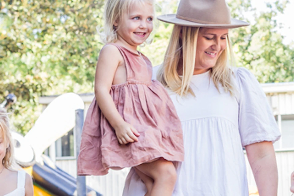 A woman in a white dress and hat walks with three young girls under an orange "Taste of Ginger Tour" banner near a gingerbread man statue.