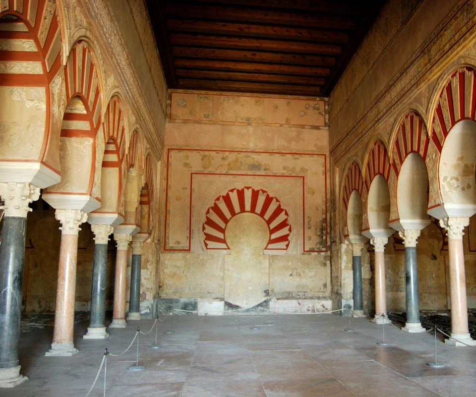 An ornate hall with red and white striped arches, detailed wall carvings, and rows of columns supporting the arches.