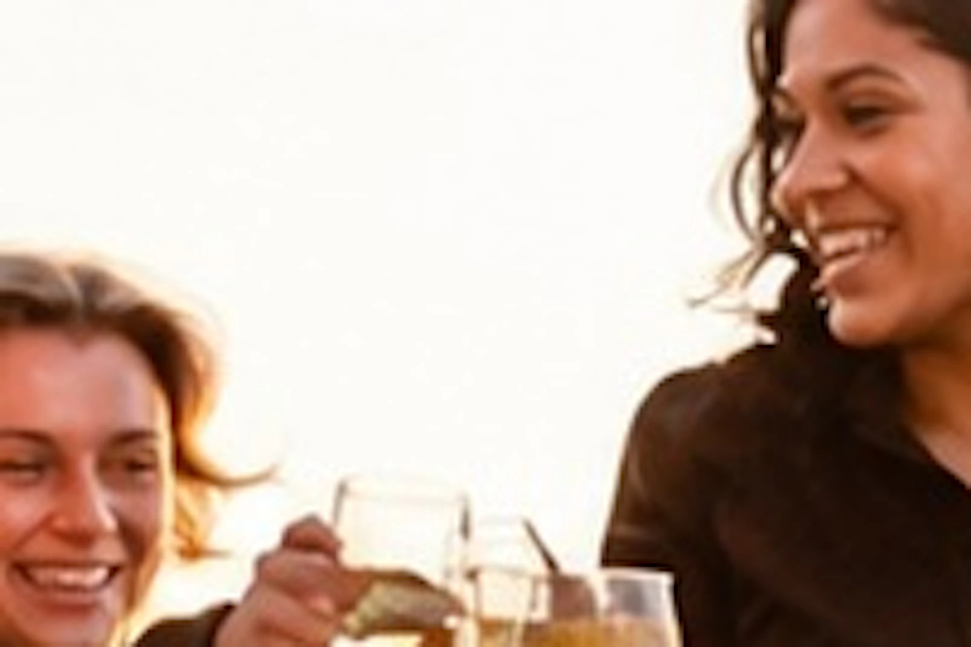 Four women standing on a rooftop terrace at sunset, clinking glasses in a celebratory toast.
