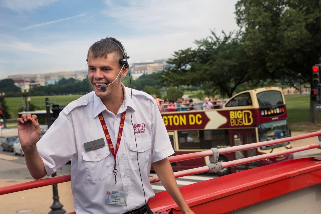 '워싱턴 D.C.' 를 배경으로 버스에서 헤드셋과 흰색 셔츠를 착용한 투어 가이드가 생동감 넘치는 연설을 하고 있습니다.