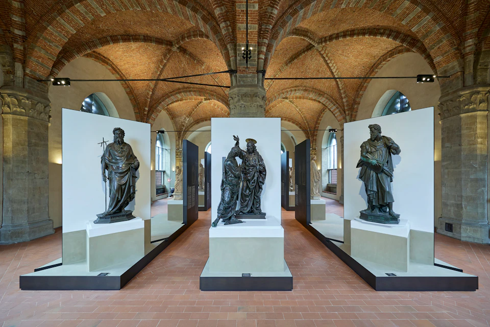 An exhibition space with statues displayed on pedestals, arched brick ceilings, and stone columns in a museum setting.