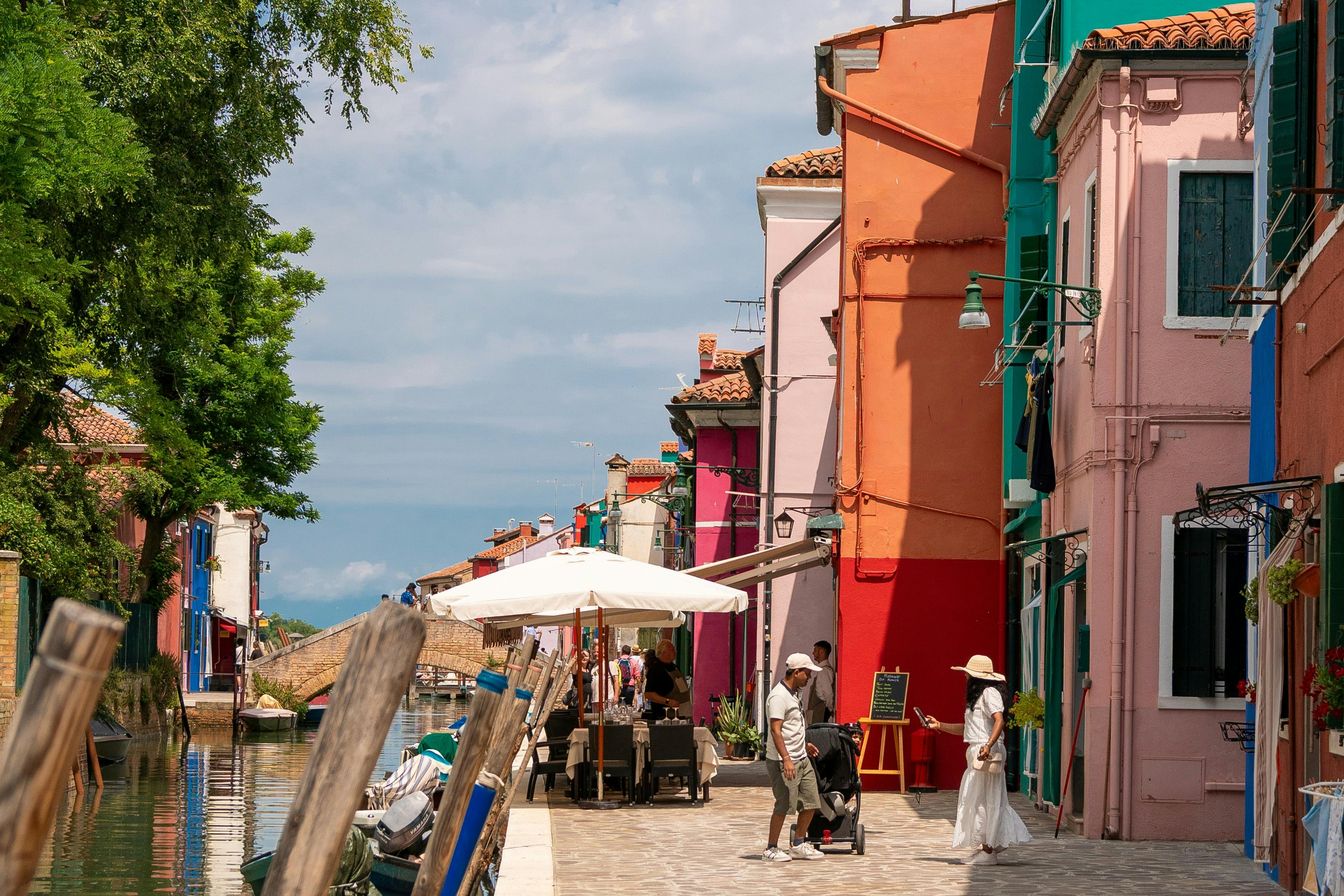 運河沿いのカラフルな通りには、活気に満ちた建物、屋外の座席、日当たりの良い雰囲気の中を歩く人々がいます。