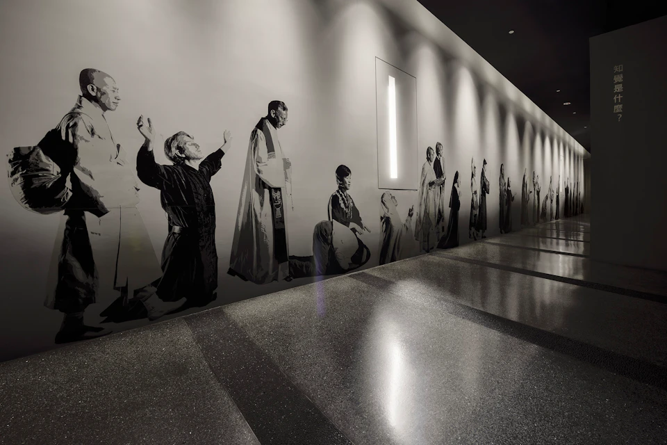 A hallway with a monochrome mural depicting various people in different poses, lit by ceiling lights.