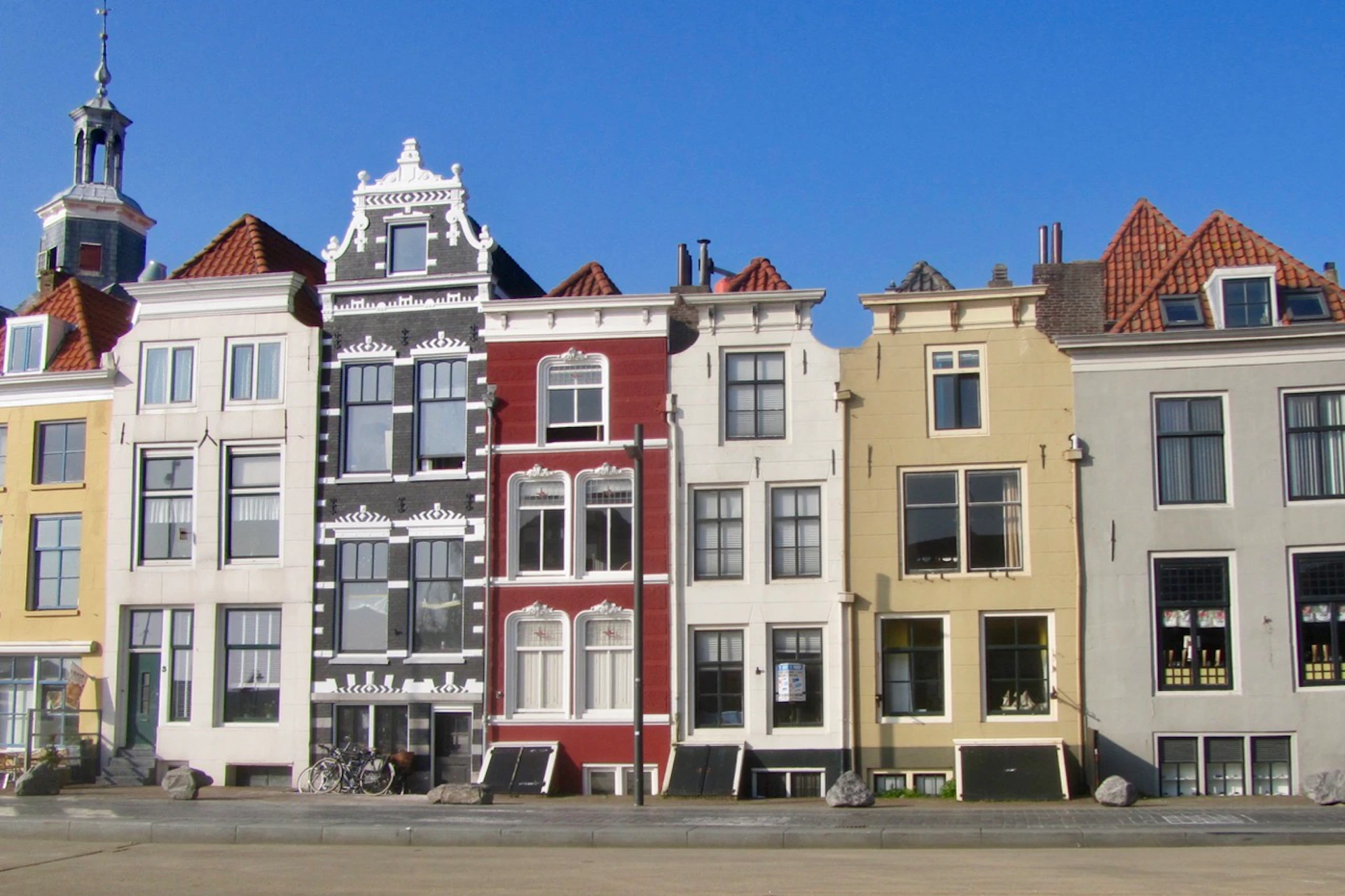 Row of four colorful, narrow buildings with ornate facades and gabled roofs on a sunny day.