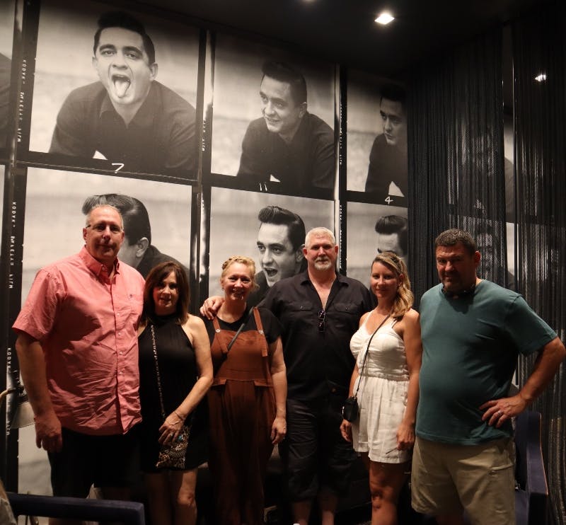 Seis personas posan delante de una pared decorada con fotos en blanco y negro de un hombre haciendo diversas expresiones faciales.