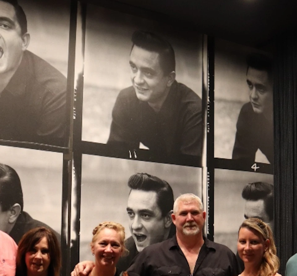 Six people posing in front of a wall decorated with black-and-white photos of a man making various facial expressions.