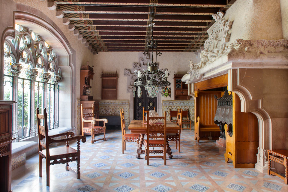 Antique dining room with ornate wooden chairs, a long table, chandeliers, a fireplace, and detailed carvings.