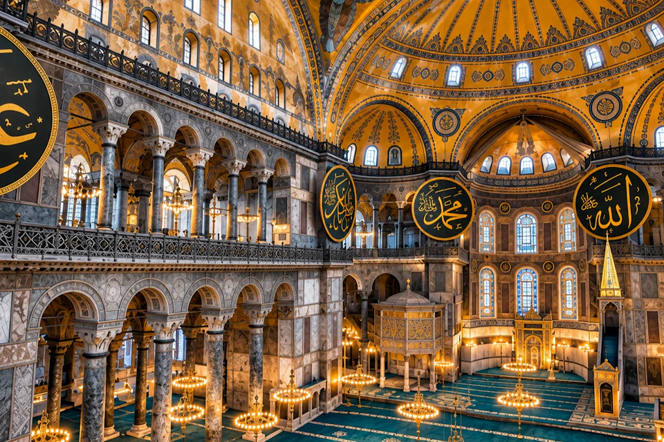 Interior of a grand historic mosque with ornate arches, large round calligraphic panels, and intricate golden domes.