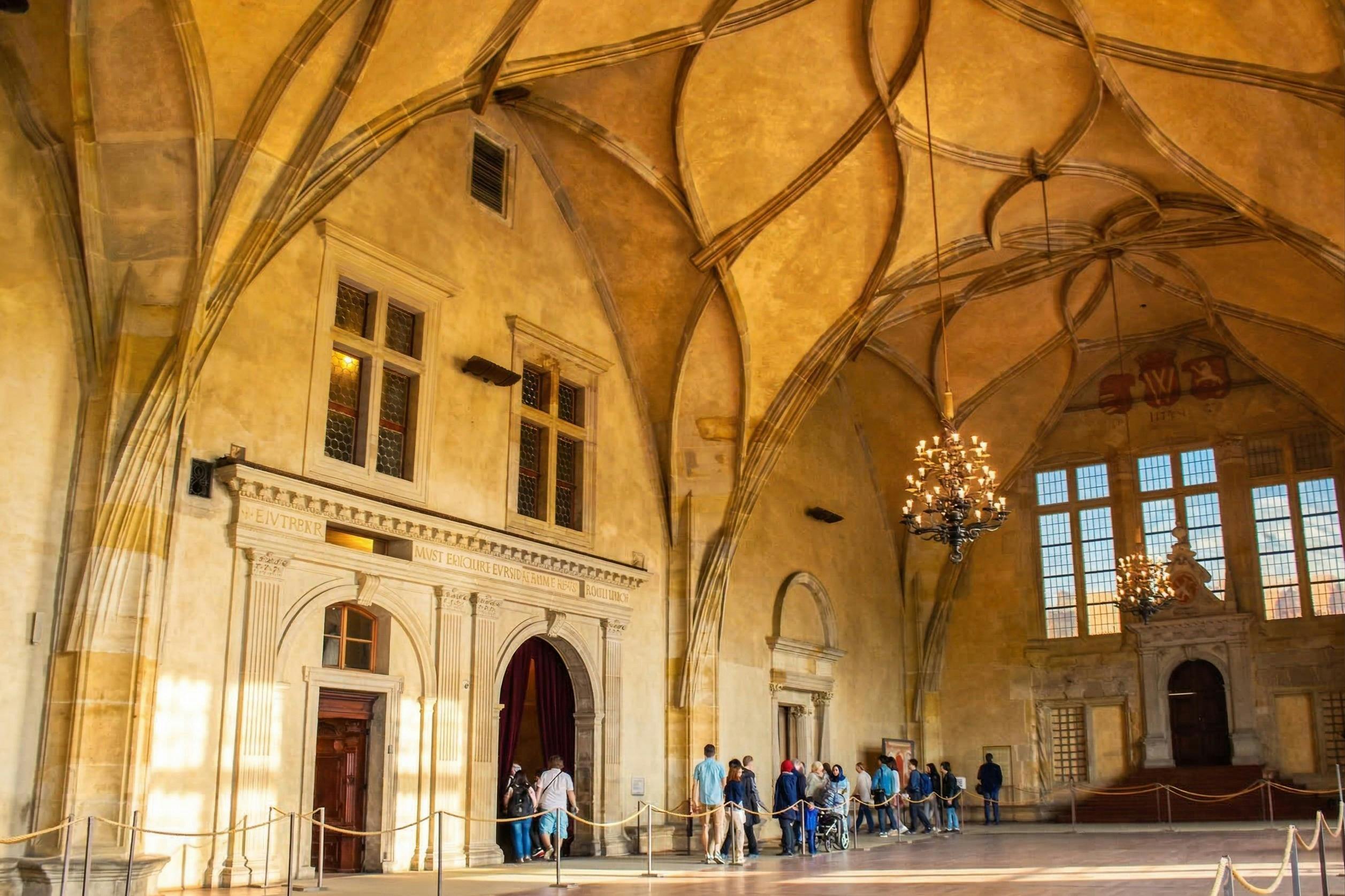 A group of people standing in a historical hall with high ceilings, intricate arches, and a chandelier.