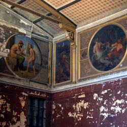 Ett rum med flagande färg, en staty och två stora, cirkulära fresker som visar mytologiska scener på de övre väggarna.