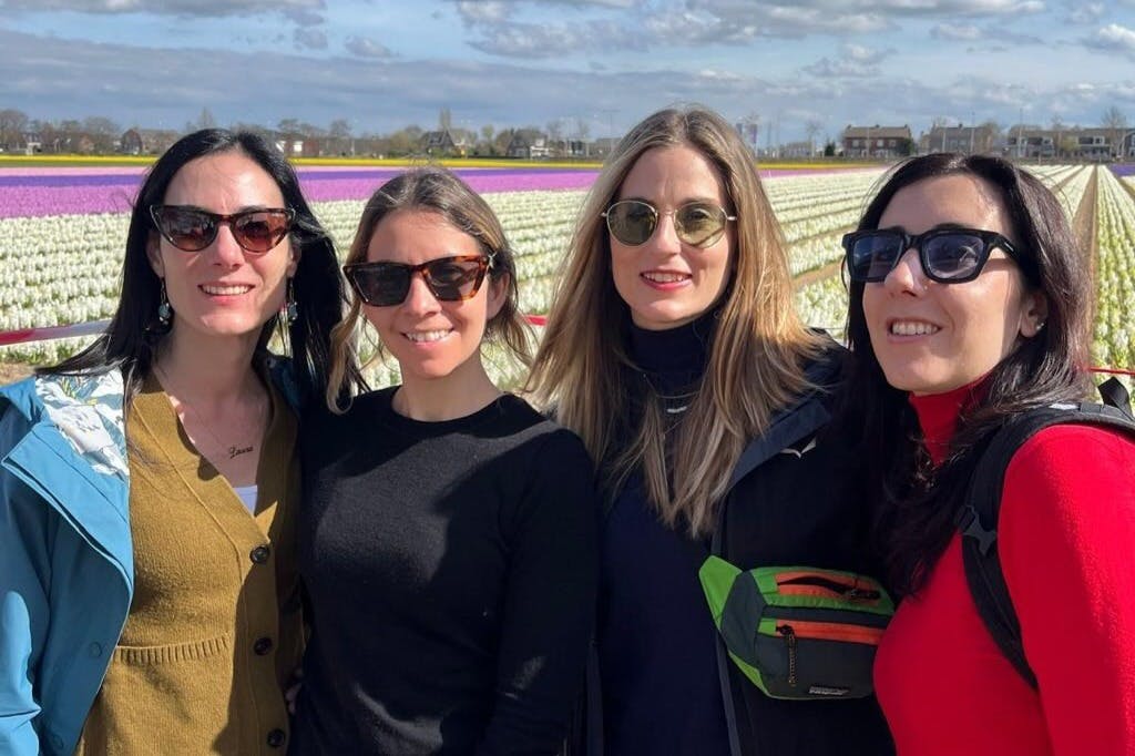 三位戴着太阳镜的女士站在一片五彩缤纷的郁金香田前，那里有一片多云的天空。