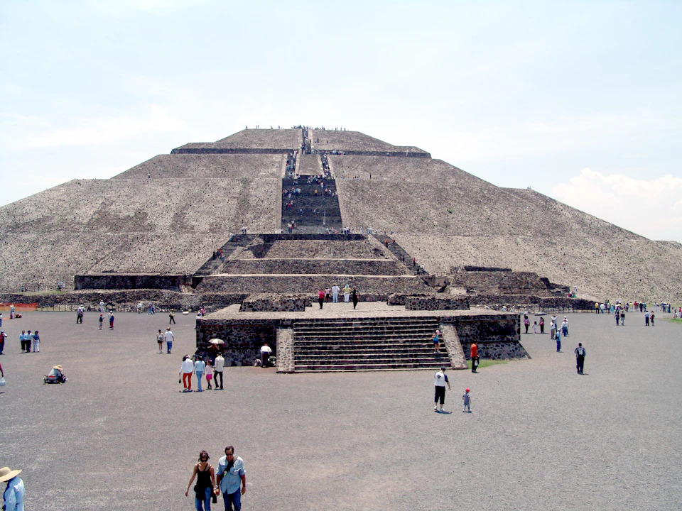 Tourists walking towards and climbing a large ancient stone pyramid under a clear sky.