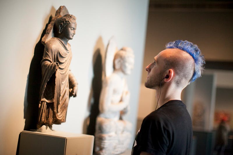 Una persona observa estàtues antigues exposades en un museu, incloent una escultura destacada de peu que representa una figura vestida.