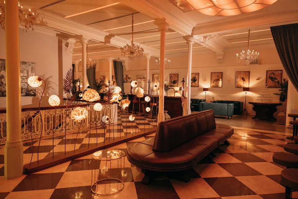 Elegant lounge with checkered floor, leather seating, chandelier lighting, and framed art on walls, illuminated by decorative lamps.