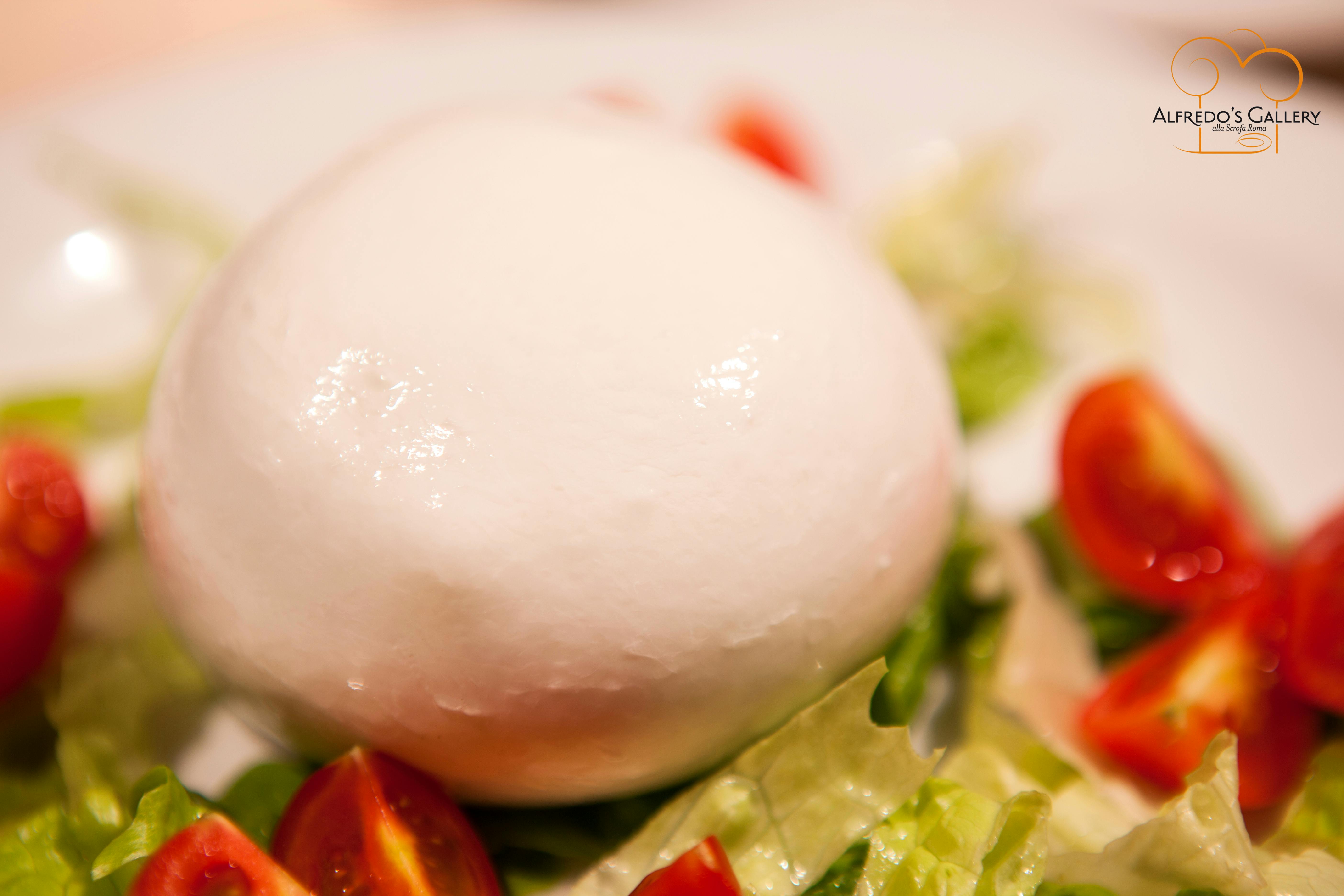 Шарик свежей моцареллы в окружении половинок помидоров черри и листьев салата.