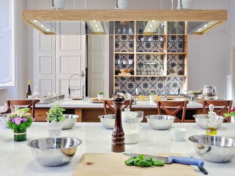 Μοντέρνα διαρρύθμιση κουζίνας με μπολ από ανοξείδωτο ατσάλι, σανίδα κοπής με ψιλοκομμένα χόρτα, μύλο πιπεριού και πλακόστρωτο backsplash.