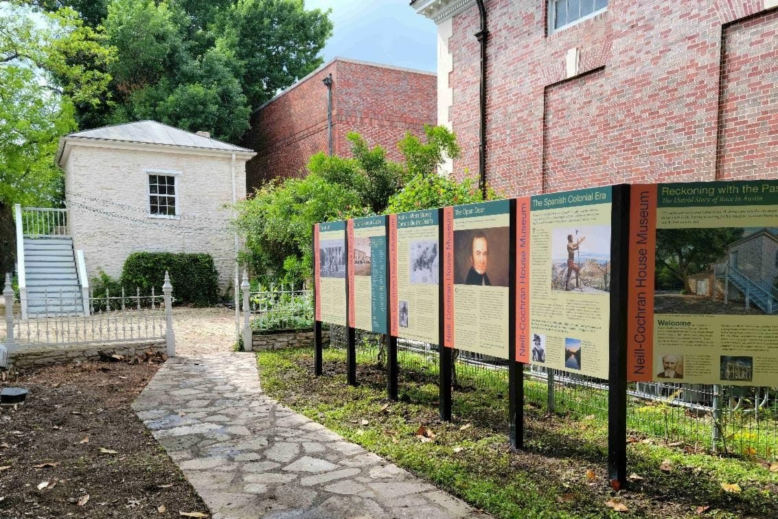 Venkovní historická expozice s informačními panely o muzeu Neil-Cochran House, obklopená zelení a budovami.