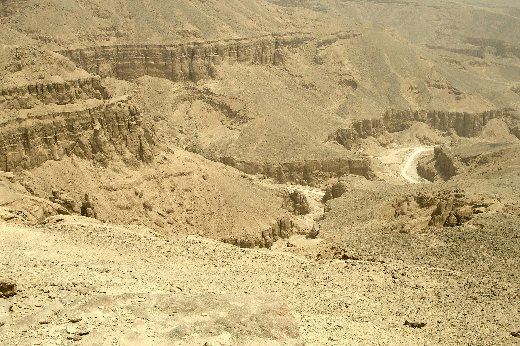 Suchá pouštní kaňonovitá krajina s členitým terénem, odhalenými skalními útvary a klikatou polní cestou v údolí.