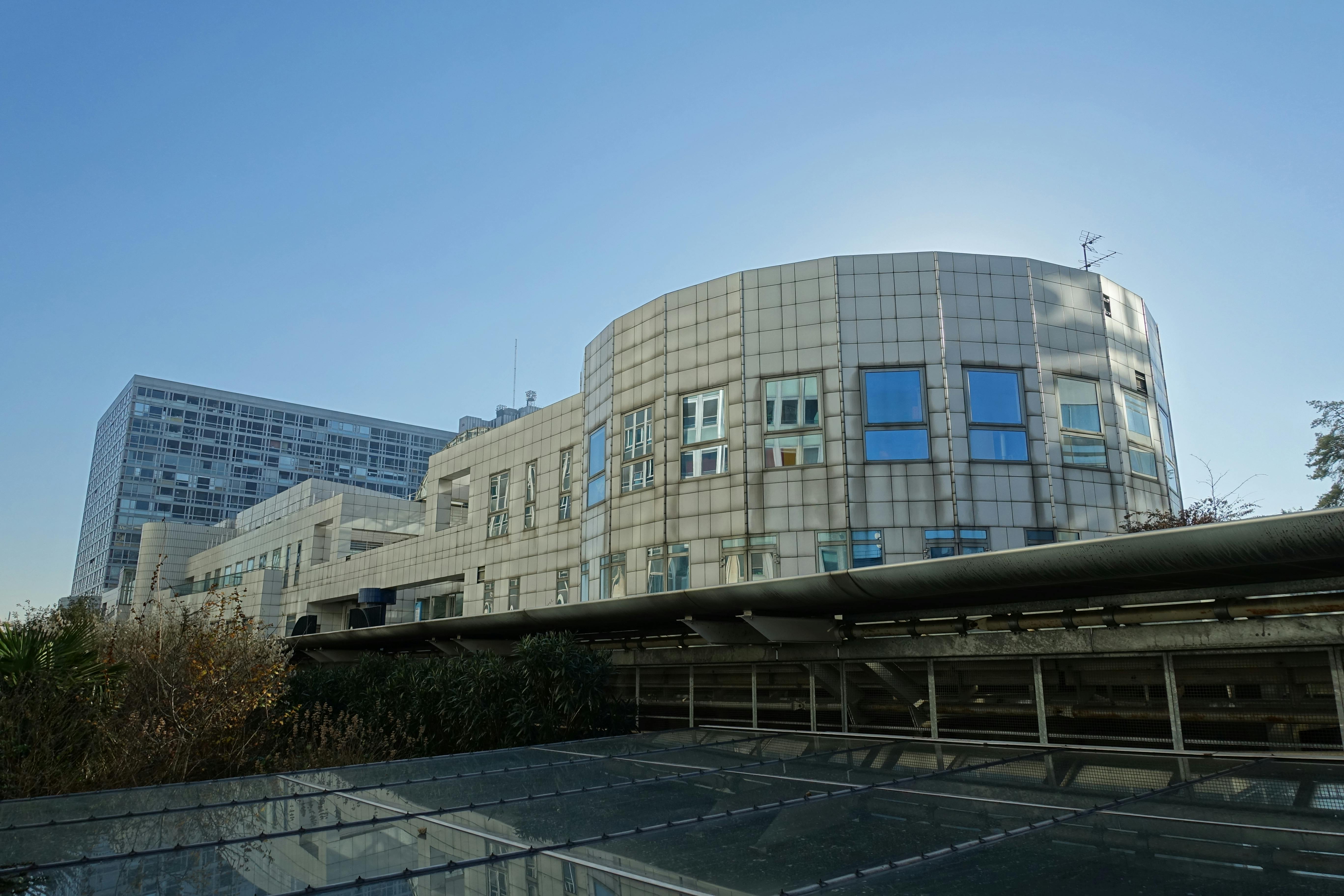 Curved modern building with large windows and rooftop greenery against a clear blue sky.