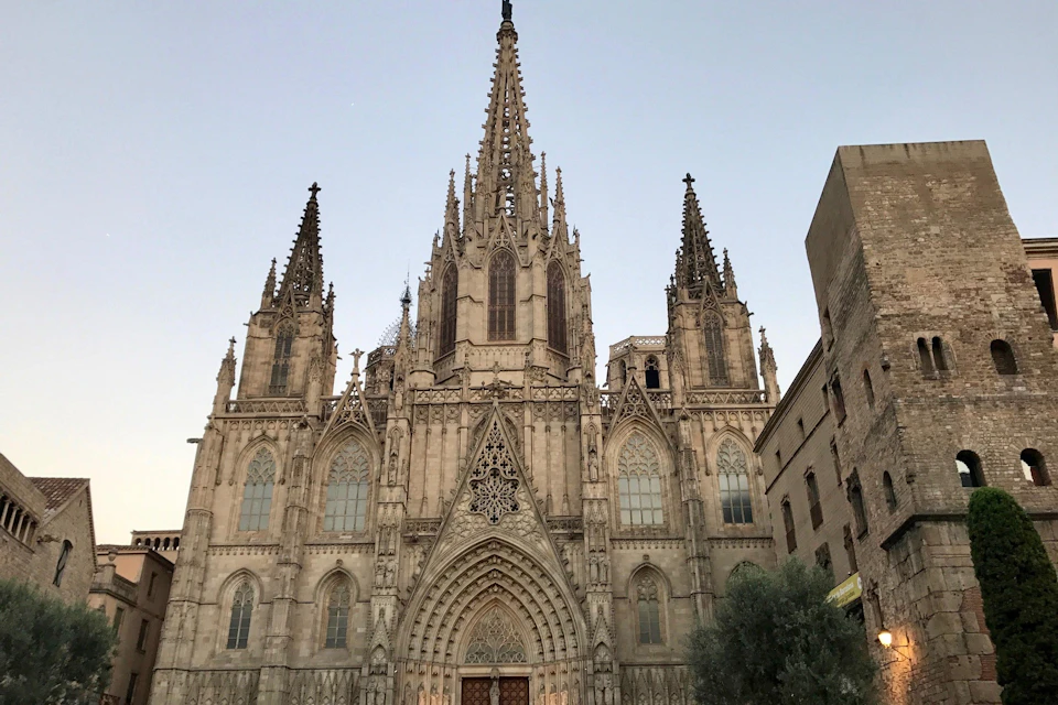 A Gothic-style cathedral with ornate spires and detailed facade, set against a clear sky, with adjacent buildings visible.