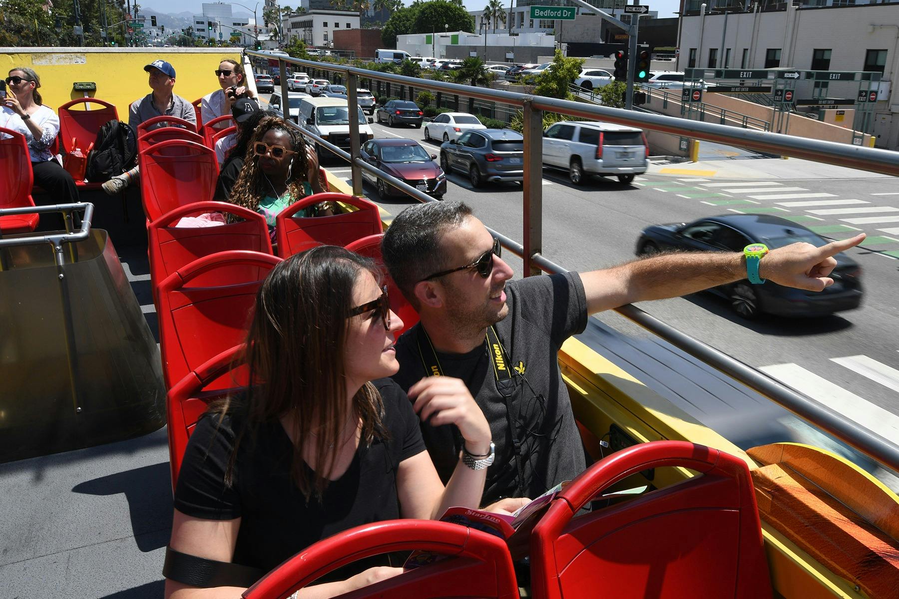 Passengers seated on the upper deck of a double-decker tour bus, enjoying the ride on a sunny day in a city.