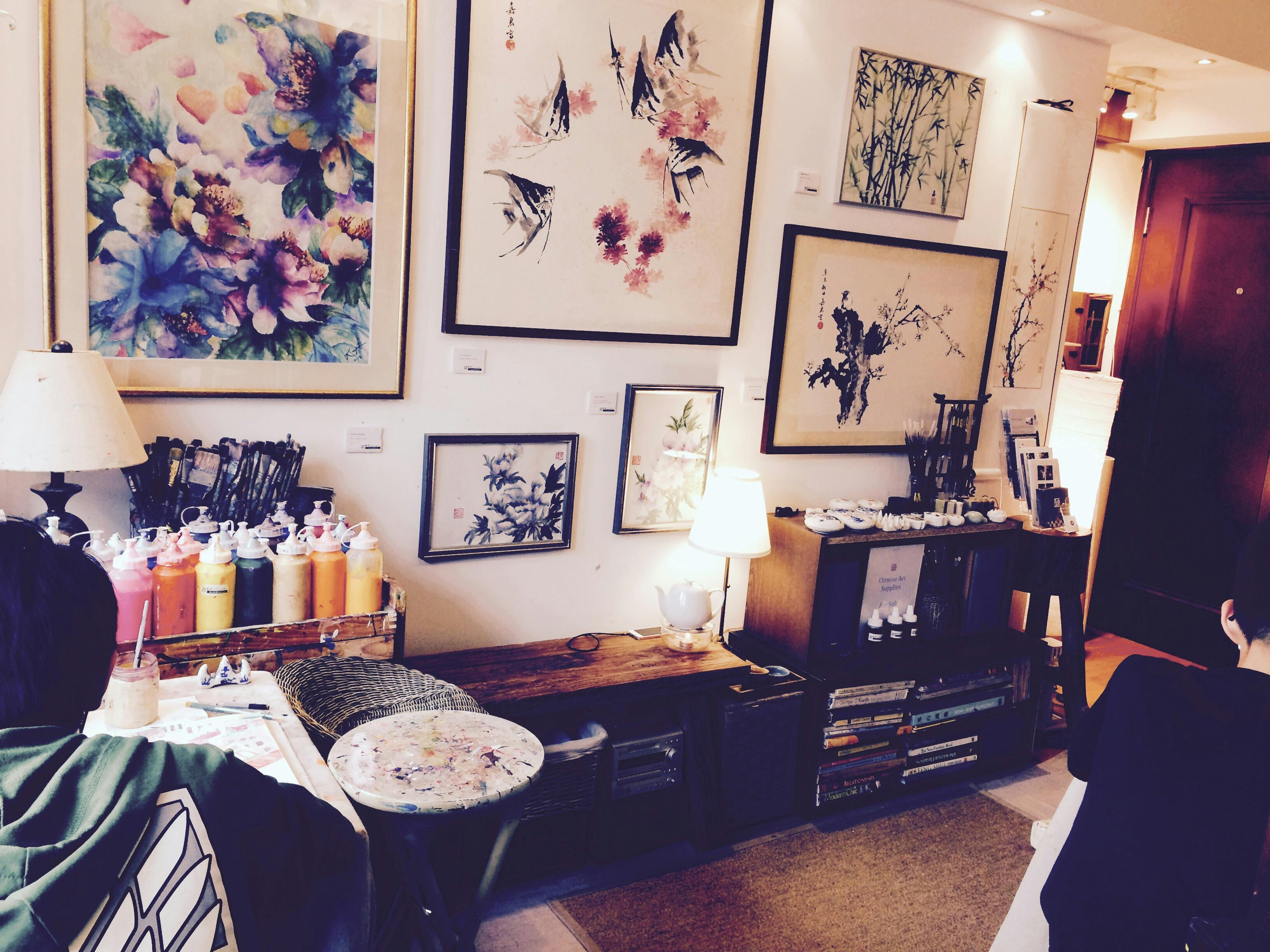 这间舒适的艺术工作室配有花卉和鸟类画框，架子上摆放着艺术用品，桌子上还有一盏小灯。