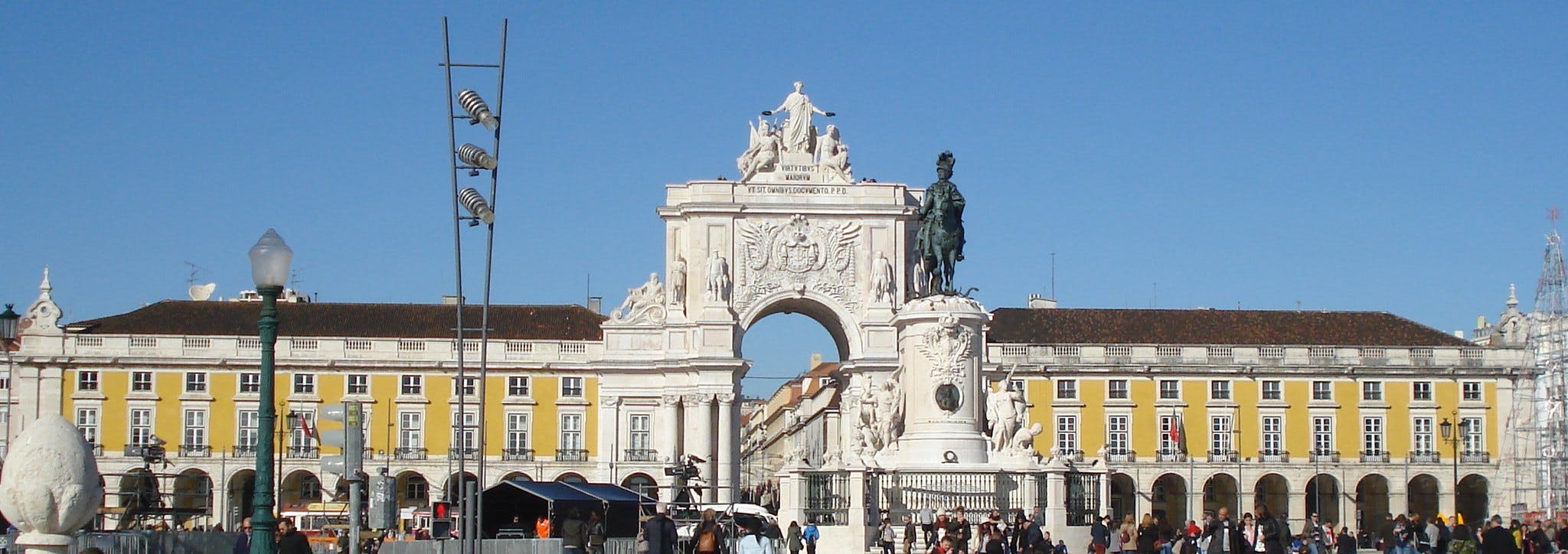 En folkmassa framför Arco da Rua Augusta, en storslagen båge med statyer i Lissabon och en staty av en man på en häst.